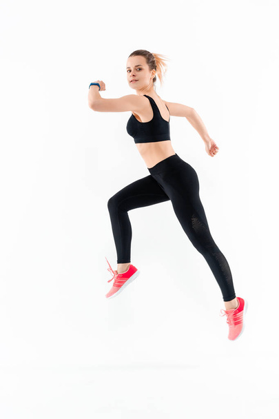 Young sporty blond woman in a black sportswear jumping isolated over white background - 写真・画像