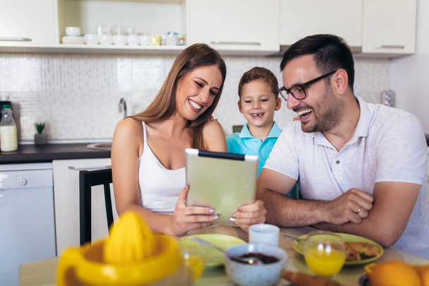 デジタルタブレットを使用して台所のテーブルで朝食を食べる家族 - 写真・画像