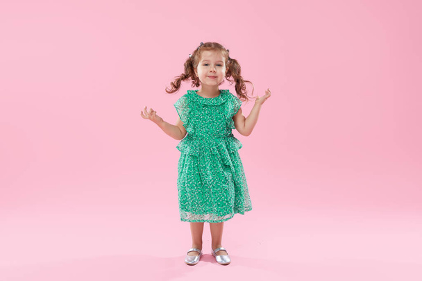 Funny little kid, toddler girl in fashionable green dress isolated on pink background - Foto, afbeelding