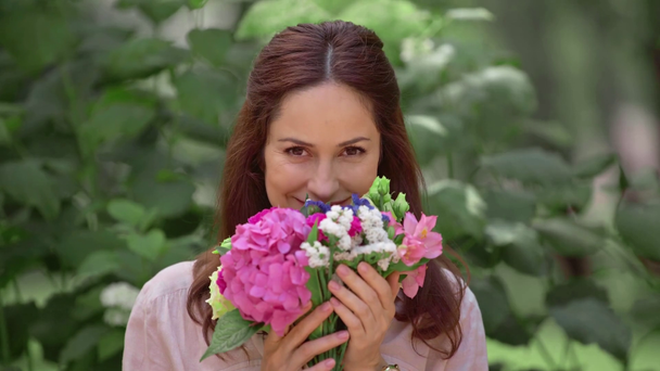 smiling woman smelling flowers in park - Felvétel, videó