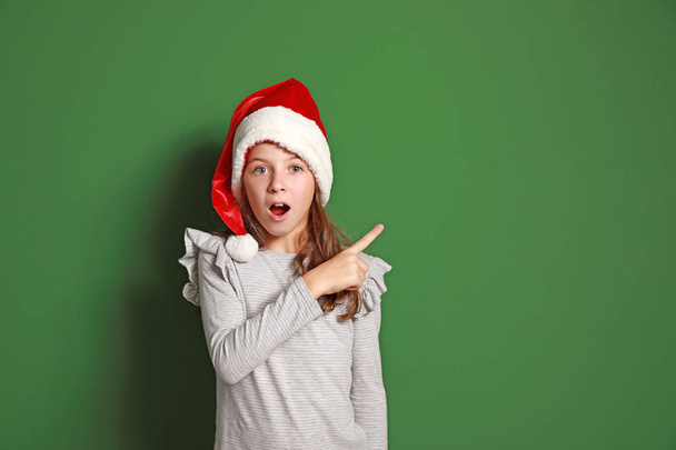 Malá překvapenej holčička v Santa Clausově klobouku ukazující na barevné pozadí - Fotografie, Obrázek