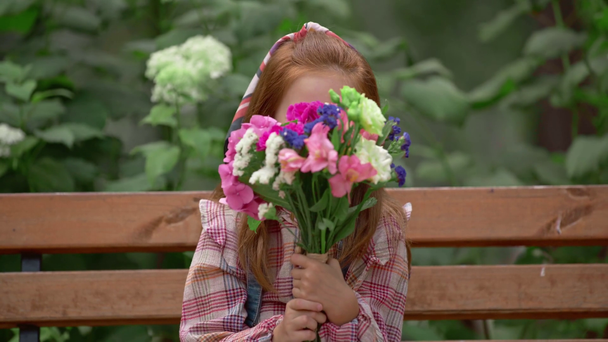 χαμογελαστός παιδί περιμένοντας κάποιον με λουλούδια στο πάρκο - Πλάνα, βίντεο