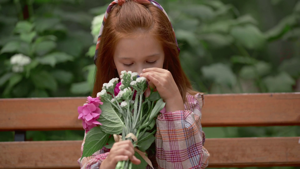 αξιολάτρευτο χαμογελαστή παιδί που μυρίζει λουλούδια στο πάρκο - Πλάνα, βίντεο