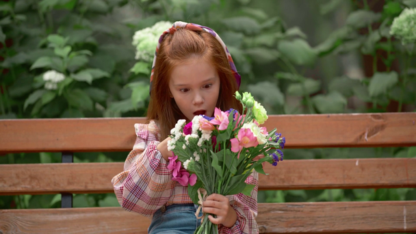 αξιολάτρευτο παιδί με λουλούδια στο πάρκο στο παγκάκι - Πλάνα, βίντεο