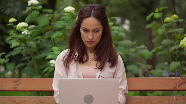 skoncentrowana kobieta za pomocą laptopa w parku - Materiał filmowy, wideo