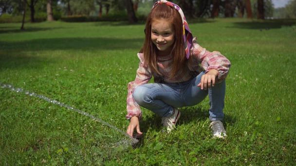 niño feliz jugando con el chorro de agua en la hierba verde
 - Metraje, vídeo
