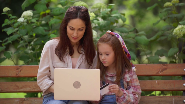 mother and daughter doing online shopping on laptop in park - Footage, Video