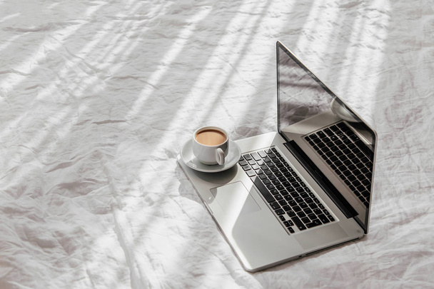 Laptop and cup of coffee on white bed. Work at home concept. Morning light  - Fotografie, Obrázek
