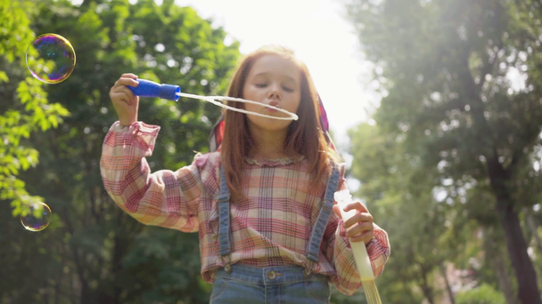 güneşli bir günde yeşil parkta sabun kabarcıkları üfleme sevimli çocuk - Video, Çekim