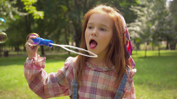 lindo pelirroja niño soplando jabón burbujas en verde parque
 - Imágenes, Vídeo