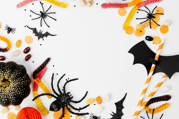 Halloween holiday frame with colorful candy, bats, spiders, pumpkins and decoration on white background. Flat lay. View from above - Foto, Imagem