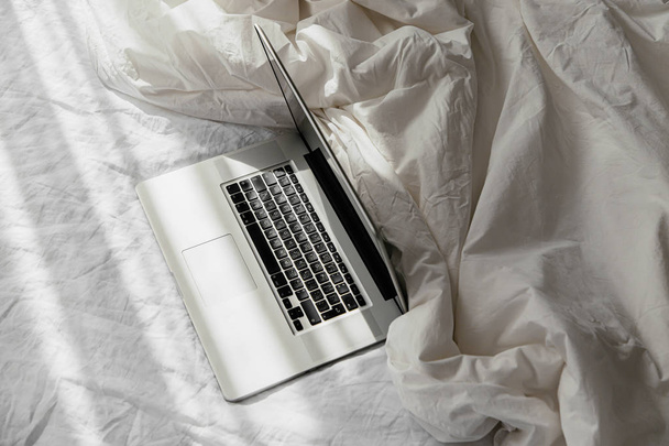 Laptop on white bed with a  blanket. Work at home concept. Morning light - Fotografie, Obrázek