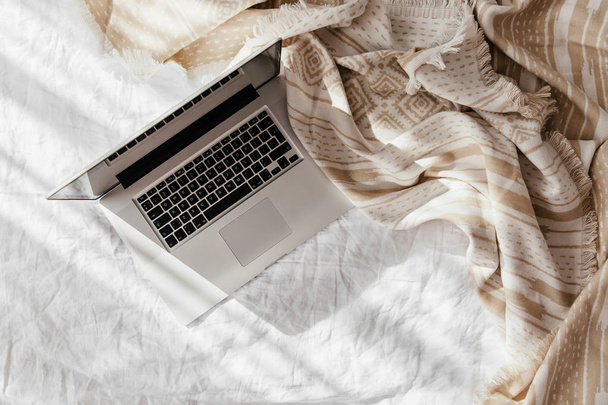 Laptop on white bed with a beige plaid. Work at home concept. Morning light  - Fotoğraf, Görsel