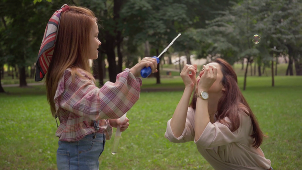 mother and daughter blowing soap bubbles in green park - Footage, Video
