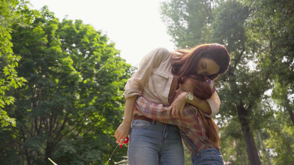 madre e hija besándose y abrazándose mientras sostienen cometa
 - Metraje, vídeo