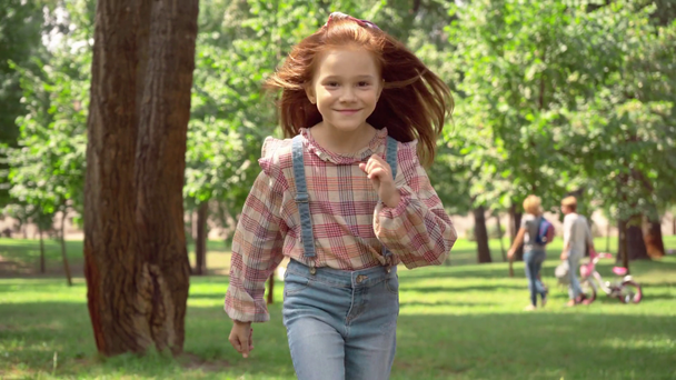 Χαριτωμένο κοκκινομάλλα παιδί τρέχει σε πράσινο ηλιόλουστο πάρκο - Πλάνα, βίντεο