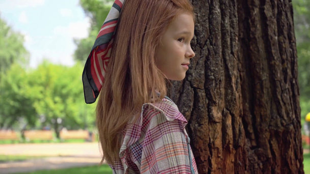 schattige roodharige kind wandelen rond boomstammen in Park - Video