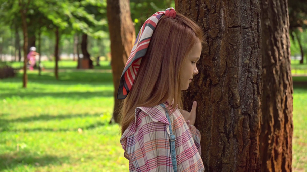 Niedliches rothaariges Kind berührt Baumstämme im Park - Filmmaterial, Video