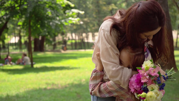 daughter gifting mother bouquet and embracing in park - Felvétel, videó