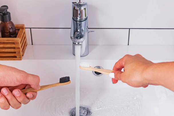Mans and womans hands close-up holding a bamboo toothbrush near the water tap - Foto, Imagem