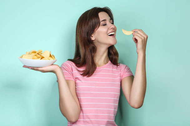 Young woman with potato chips in plate on mint background - Foto, Bild