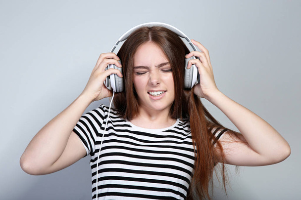 Young beautiful woman with headphones on grey background - Fotoğraf, Görsel