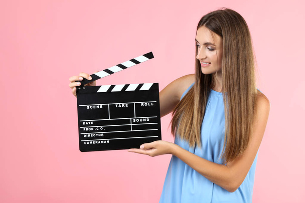 Young woman with black clapper board on pink background - Foto, Bild