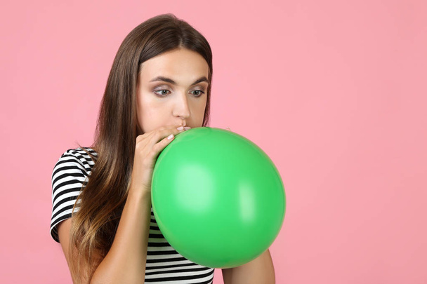 Young woman blowing green balloon on pink background - 写真・画像