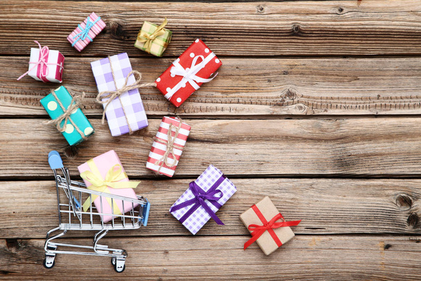 Small shopping cart with gift boxes on brown wooden table - Фото, зображення