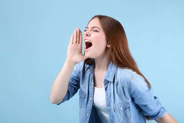 Young beautiful woman screaming on blue background - Photo, Image