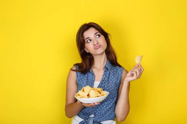Young woman with potato chips in plate on yellow background - Foto, afbeelding