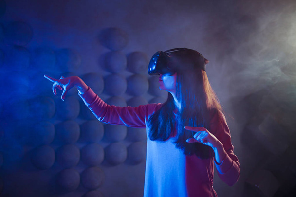 A surprised woman in virtual reality glasses touches the air, tries to find something, uses an invisible control panel. - Photo, Image