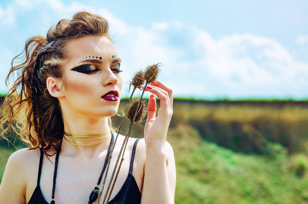 Porträt eines Mädchens mit aggressivem Make-up amazon wiking presst stachelige Blumen Distel auf ihr Gesicht. - Foto, Bild