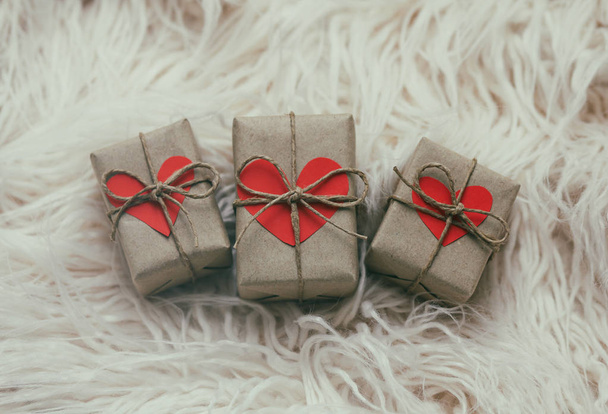 Set of gift boxes wrapped in craft paper and tie hemp string. With cardboard hearts. White fur background. - Zdjęcie, obraz