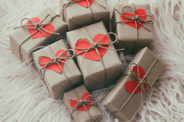 Set of gift boxes wrapped in craft paper and tie hemp string. With cardboard hearts. White fur background. - Foto, Imagem