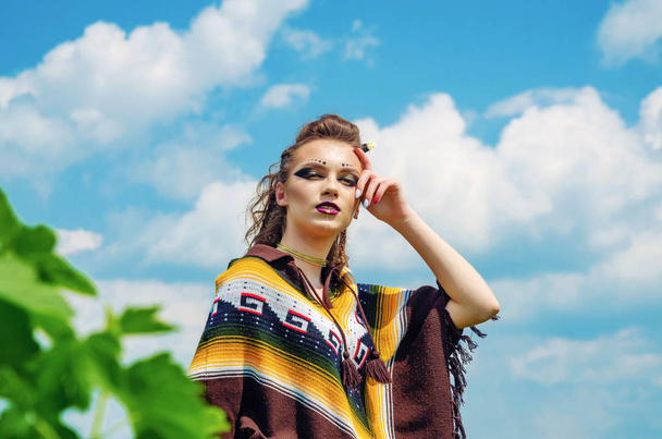 Portrét dívky s make-upem Amazonka, Viking, agresivní válečné barvy. Oblečen v Ponchu na pozadí oblohy. - Fotografie, Obrázek