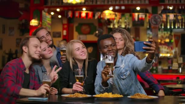 Znajomi biorą selfie ze smartfonem w barze. Młodzi ludzie pozują, śmieją się i rozmawiają. Butelki piwa i. znajomi biorą selfie ze smartfonem w. - Materiał filmowy, wideo