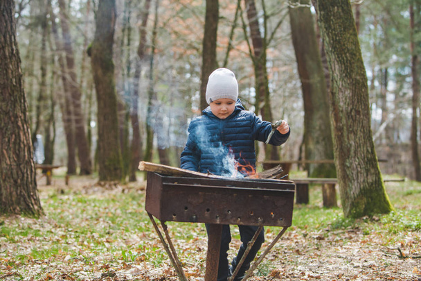 μικρό αγόρι παιδί βάλει κλαδιά σε φωτιά σε σχάρα - Φωτογραφία, εικόνα