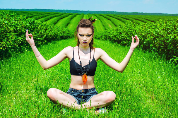Viking aggressive makeup girl cosplay in a green wheat field. Kneeling, praying to the ancient gods. Paganism, feminism, independence, tribe. - Photo, Image
