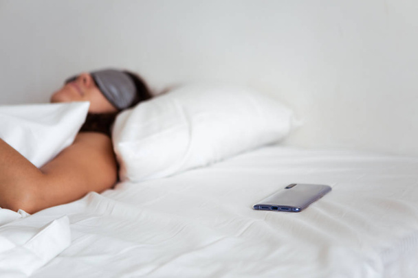woman sleeping in sleep mask smartphone near her - Фото, изображение
