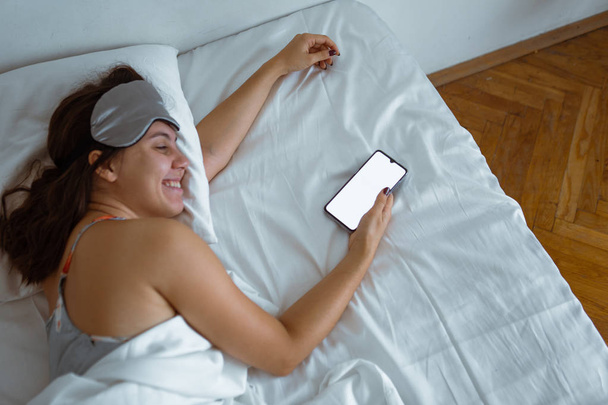 mujer despierta mirando en la pantalla blanca del teléfono inteligente
 - Foto, Imagen