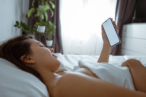 Frau mit Smartphone im Bett mit weißen Laken - Foto, Bild