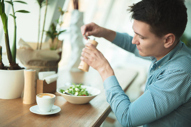 young handsome man eats salad and drinks coffee for lunch during break at cafe near office - 写真・画像