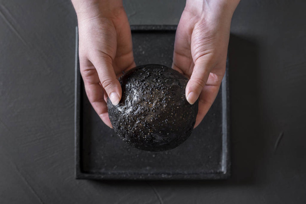 Black bread bun held in hands. Strange food - Zdjęcie, obraz
