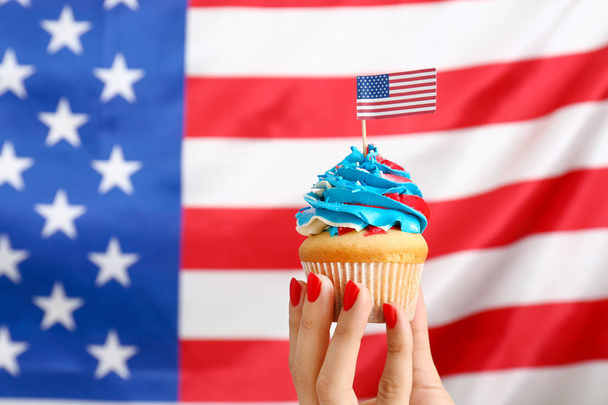 Female hand with tasty patriotic cupcake against USA flag - Фото, зображення