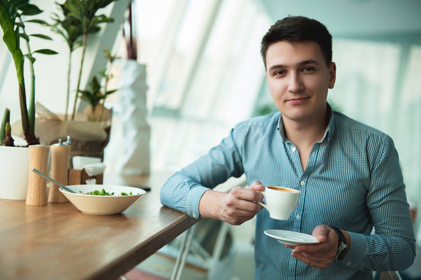 jeune homme beau boire son café chaud et manger de la salade pour le déjeuner pendant la pause au café à la mode près du bureau semble satisfait
 - Photo, image