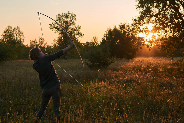 A woman shoots a bow in nature at sunset. - Фото, зображення