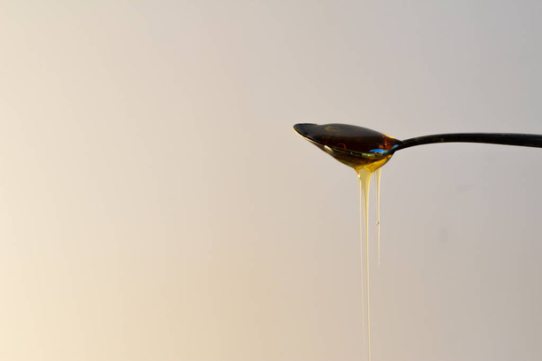 Honey dripping from spoon against a white background. - Φωτογραφία, εικόνα