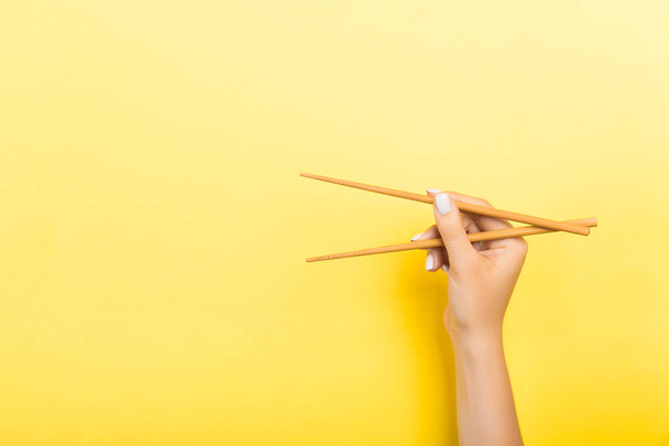 Wooden chopsticks holded with female hands on yellow background. Ready for eating concepts with empty space - Fotó, kép