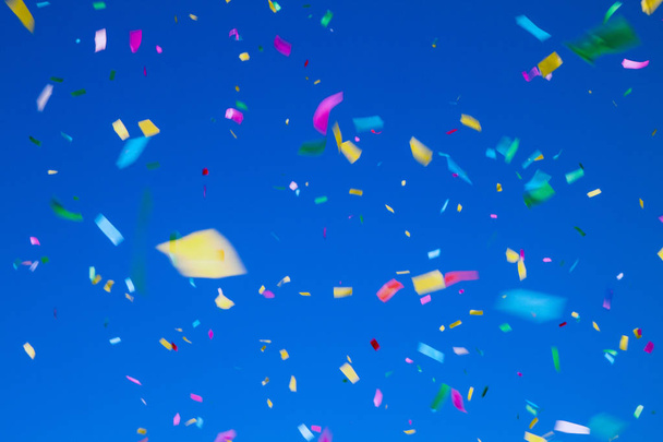 multicolored confetti on clear blue sky background. Concept of holiday backdrop - Zdjęcie, obraz